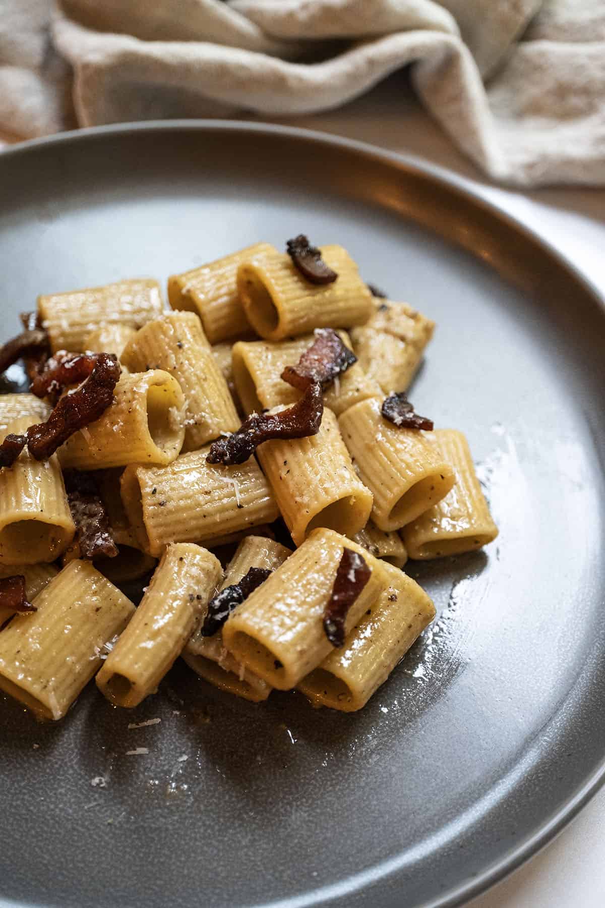 Pasta alla gricia served on a plate and topped with guanciale. 