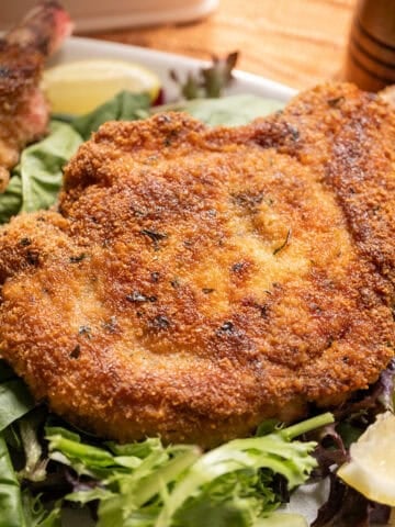 Pork chop milanese over a greens salad and a wedge of lemon on the side.