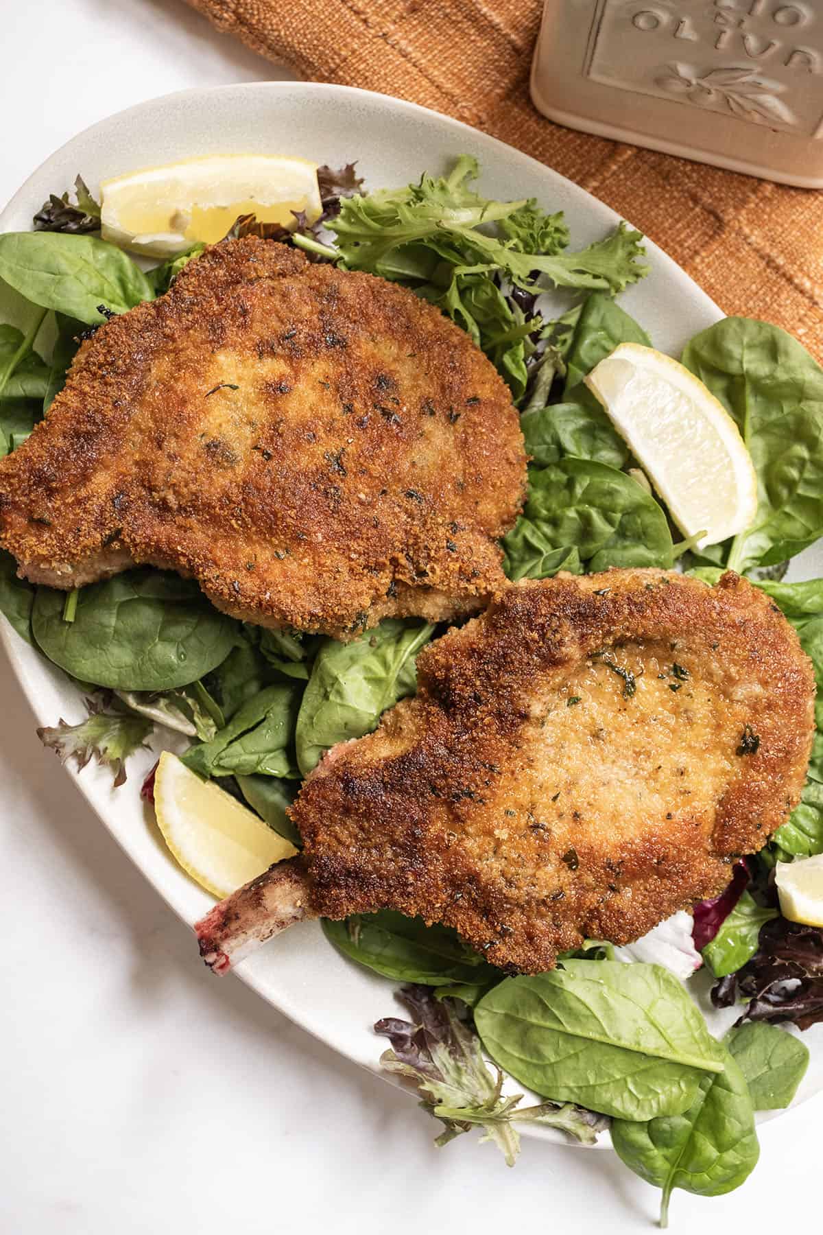 Pork chop milanese over a greens salad and a wedge of lemon on the side.