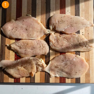 Tenderized chicken breast seasoned with salt and pepper on a cutting board.
