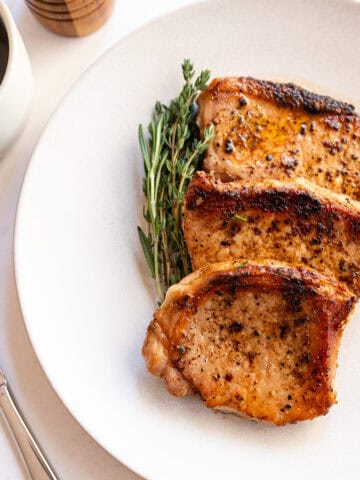 Boneless pork chops cooked on a plate with rosemary and thyme