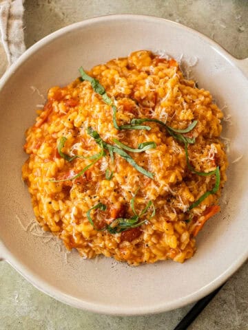 Creamy cherry tomato risotto in a bowl topped with fresh basil.