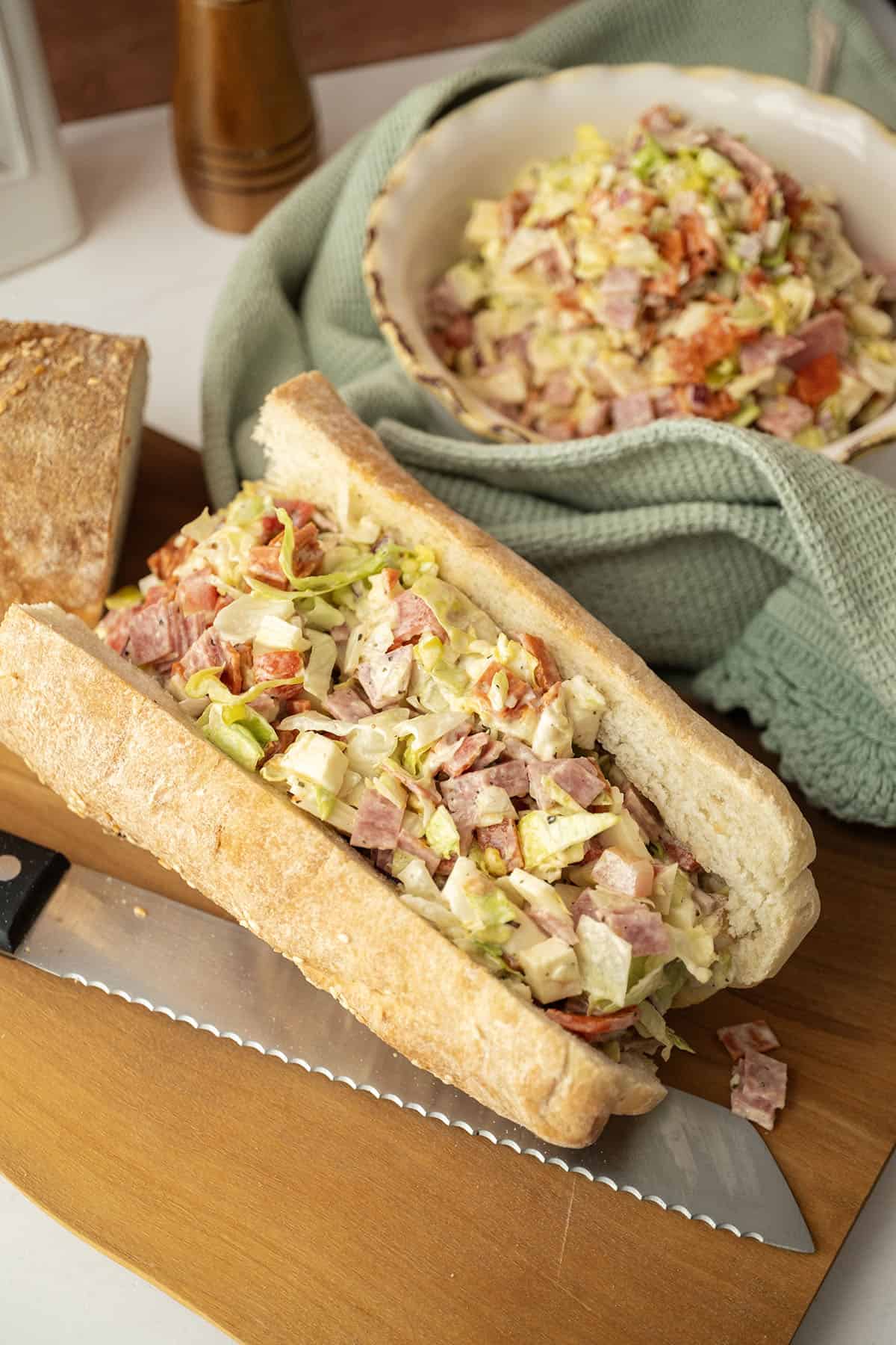 Chopped Italian salad in an sandwich roll with a bowl of the salad behind.