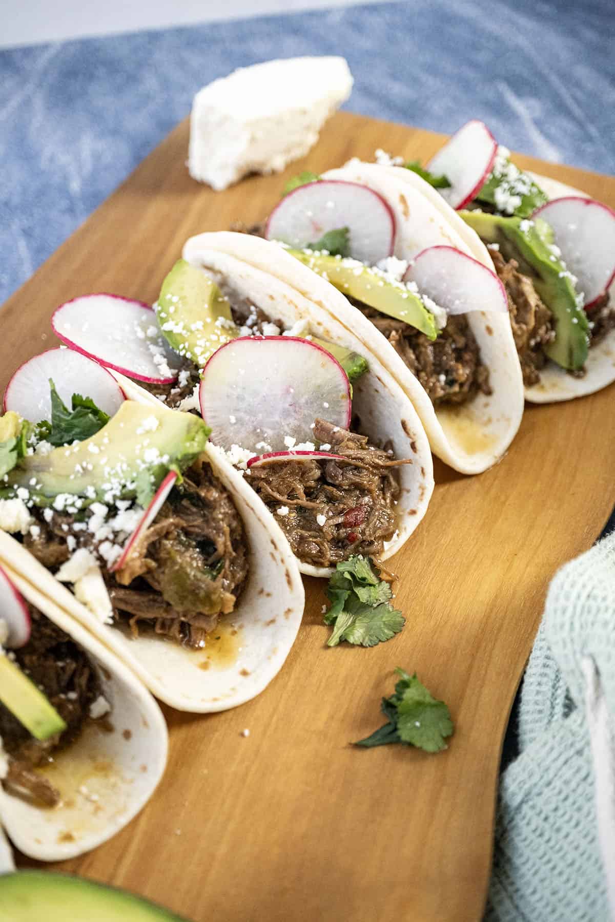Beef barbacoa tacos with sliced radish, avocado, and cotija cheese.
