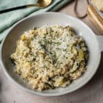 Zucchini risotto in a bowl topped with parmigiano and parsley.
