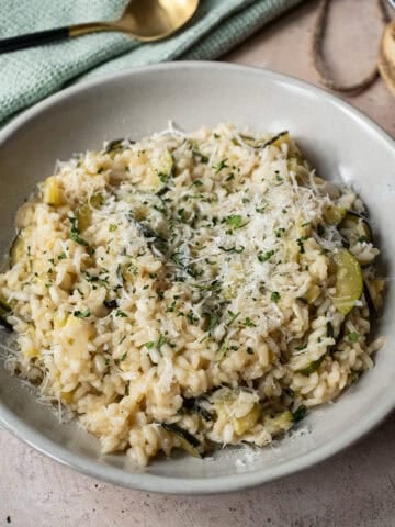 Zucchini risotto in a bowl topped with parmigiano and parsley.