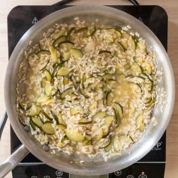 Chicken broth absorbing into rice in saucepan.