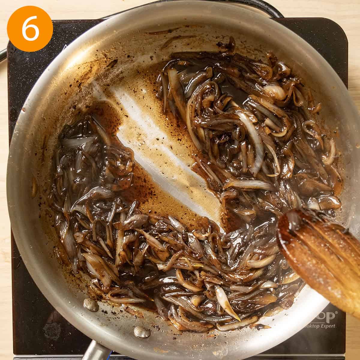 Onion jam finished in a pan, with spoon dragged through sauce to show thickness of sauce. 