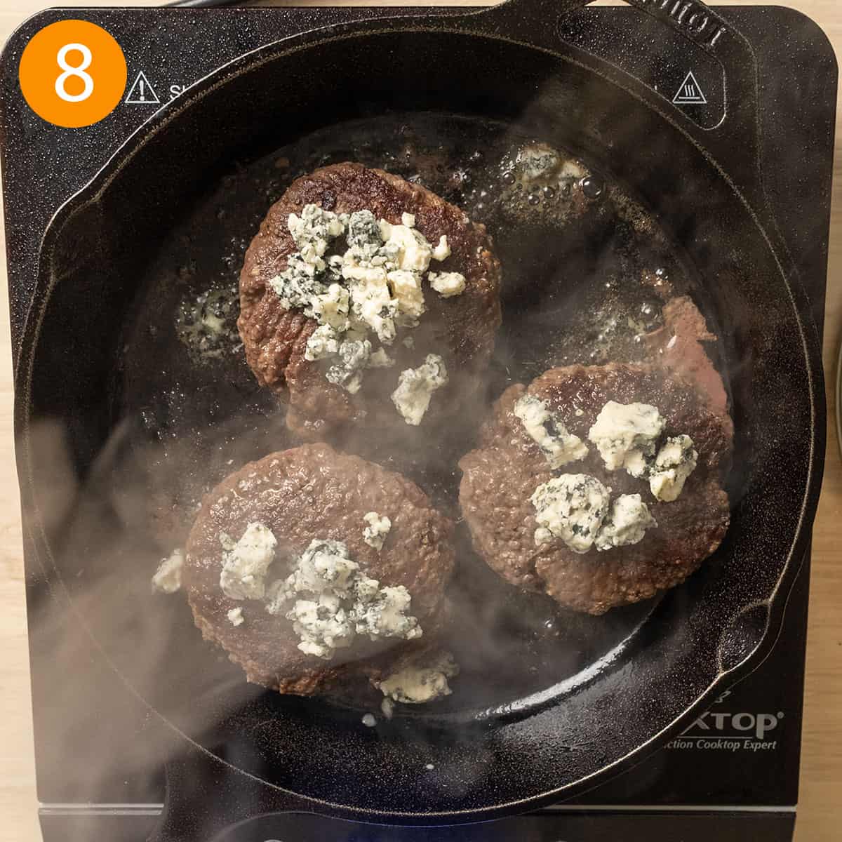 Grilling burgers with blue cheese crumbles on top.
