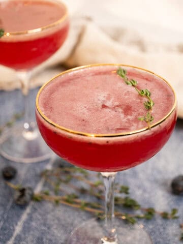 2 Blueberry mocktails with a sprig of thyme garnish in a glass.