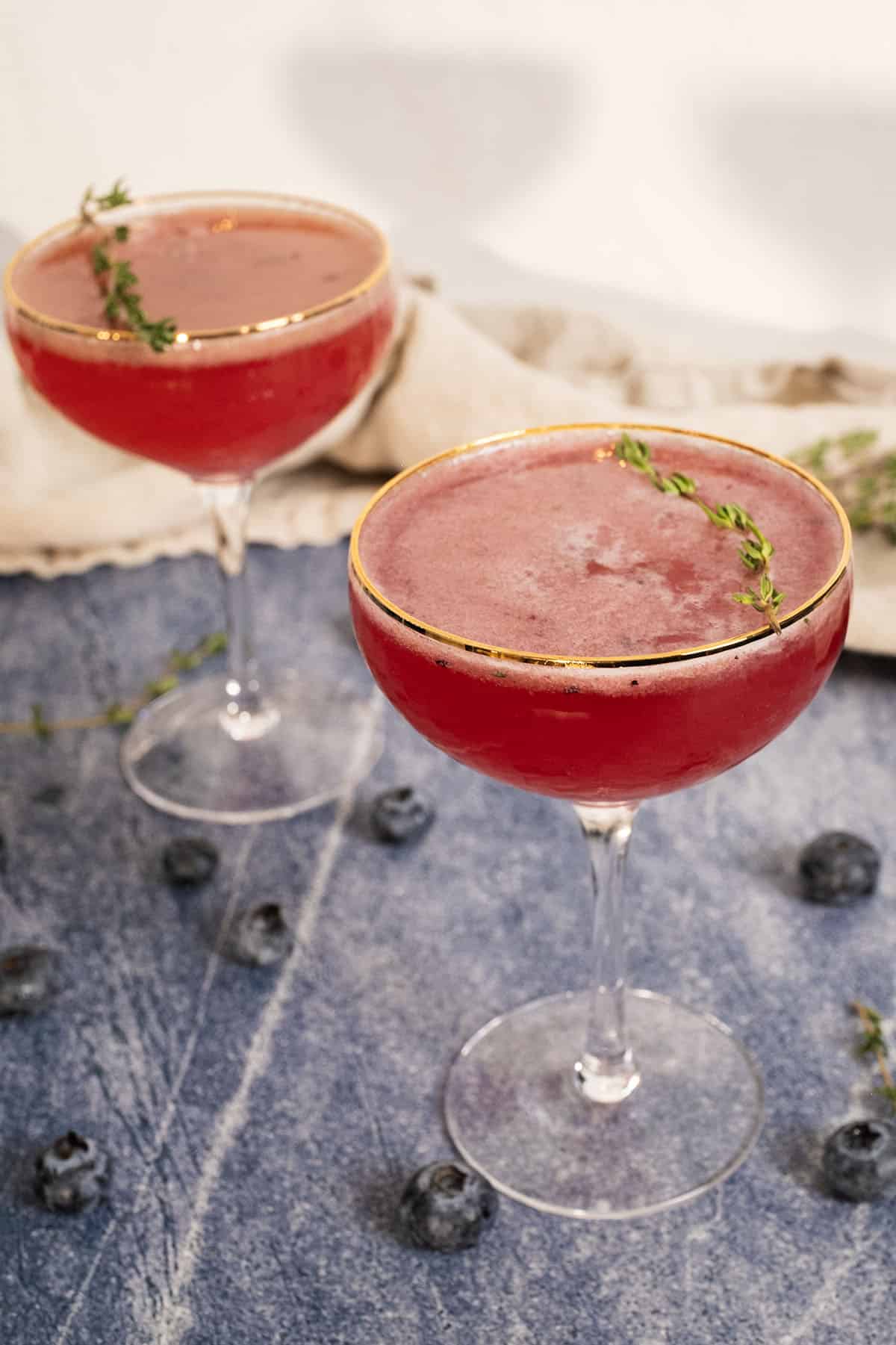2 Blueberry mocktails with a sprig of thyme garnish in a glass.