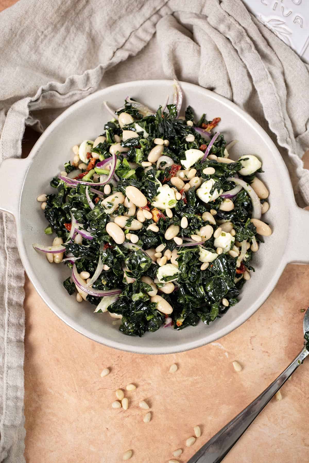 Kale and Cannellini Bean salad in a bowl topped with pine nuts.