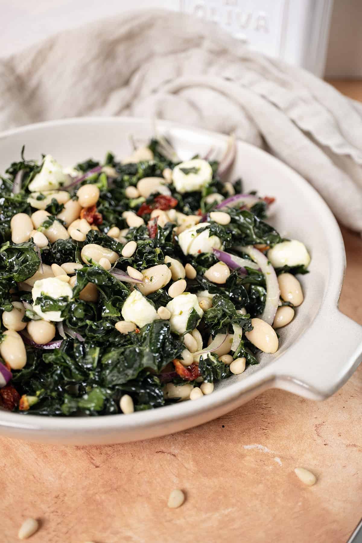 Kale and Cannellini Bean salad in a bowl topped with pine nuts.