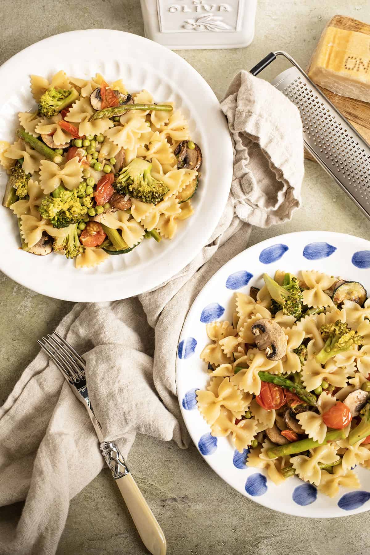 2 bowls filled with pasta primavera and a side of parmesan cheese.