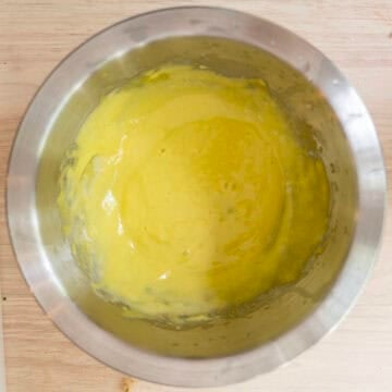 Pale yellow garlic aioli whisked together in a bowl.