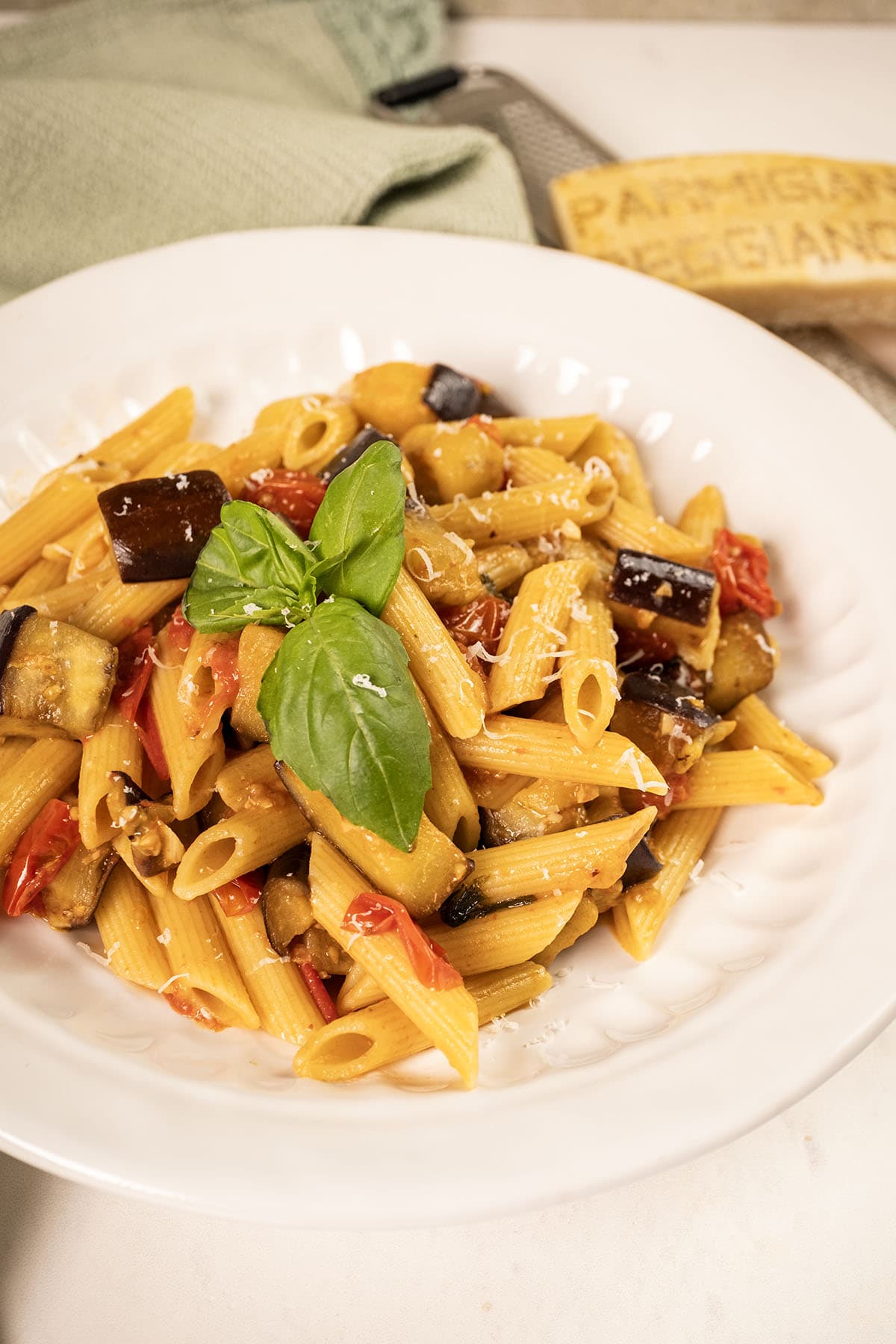 Pasta with eggplant and cherry tomatoes in a bowl garnished with fresh basil.