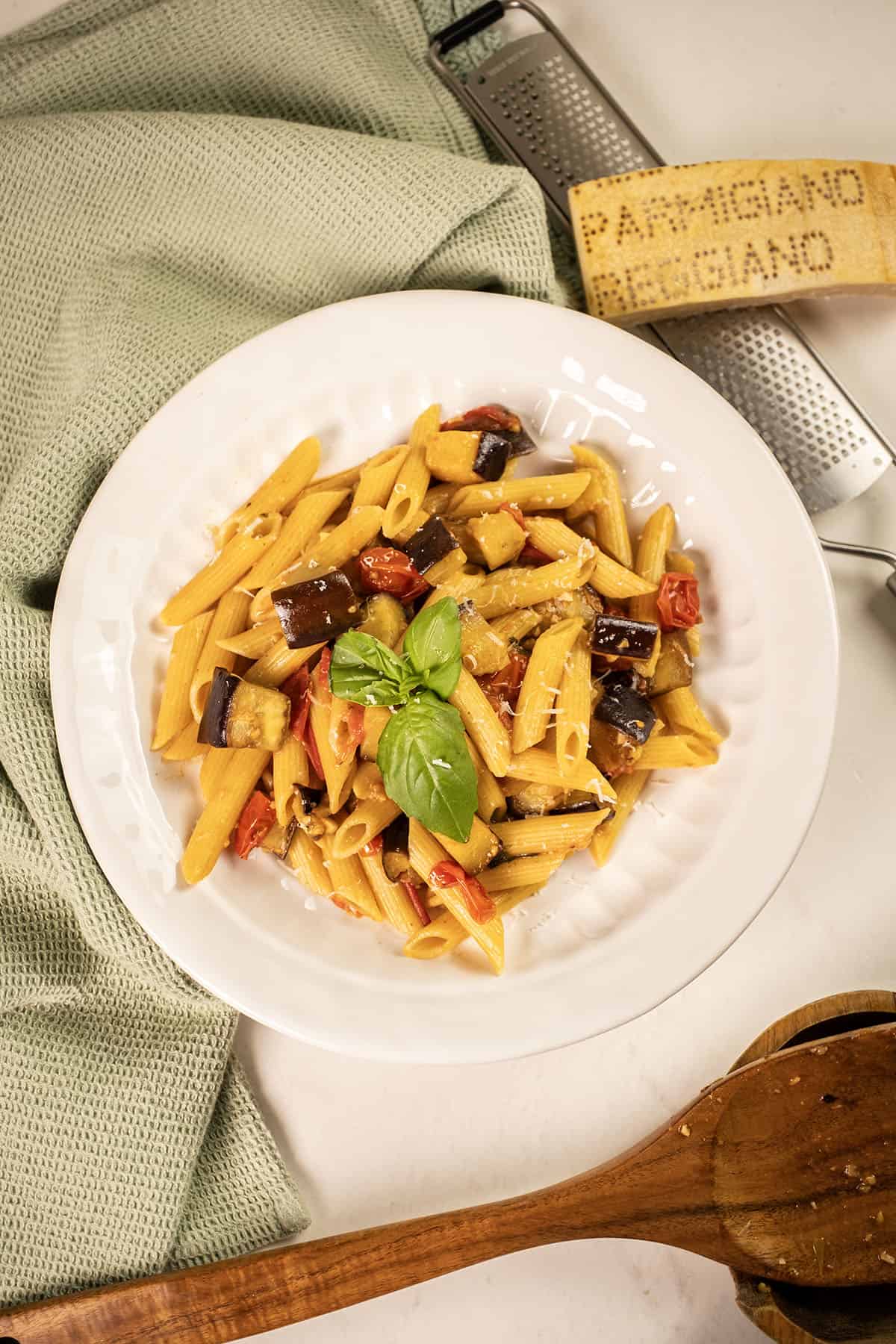 Pasta with eggplant and cherry tomatoes in a bowl garnished with fresh basil.