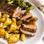 Sliced pork tenderloin served on a plate with roasted potatoes and broccoli.