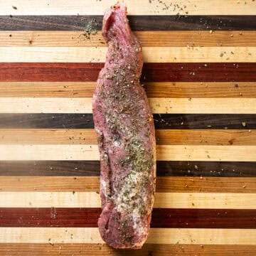 Seasoned pork tenderloin on a cutting board.