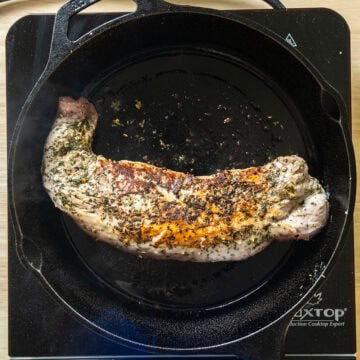 Pork tenderloin flipped on cast iron pan searing other side.