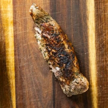 Cooked pork tenderloin resting on a cutting board.