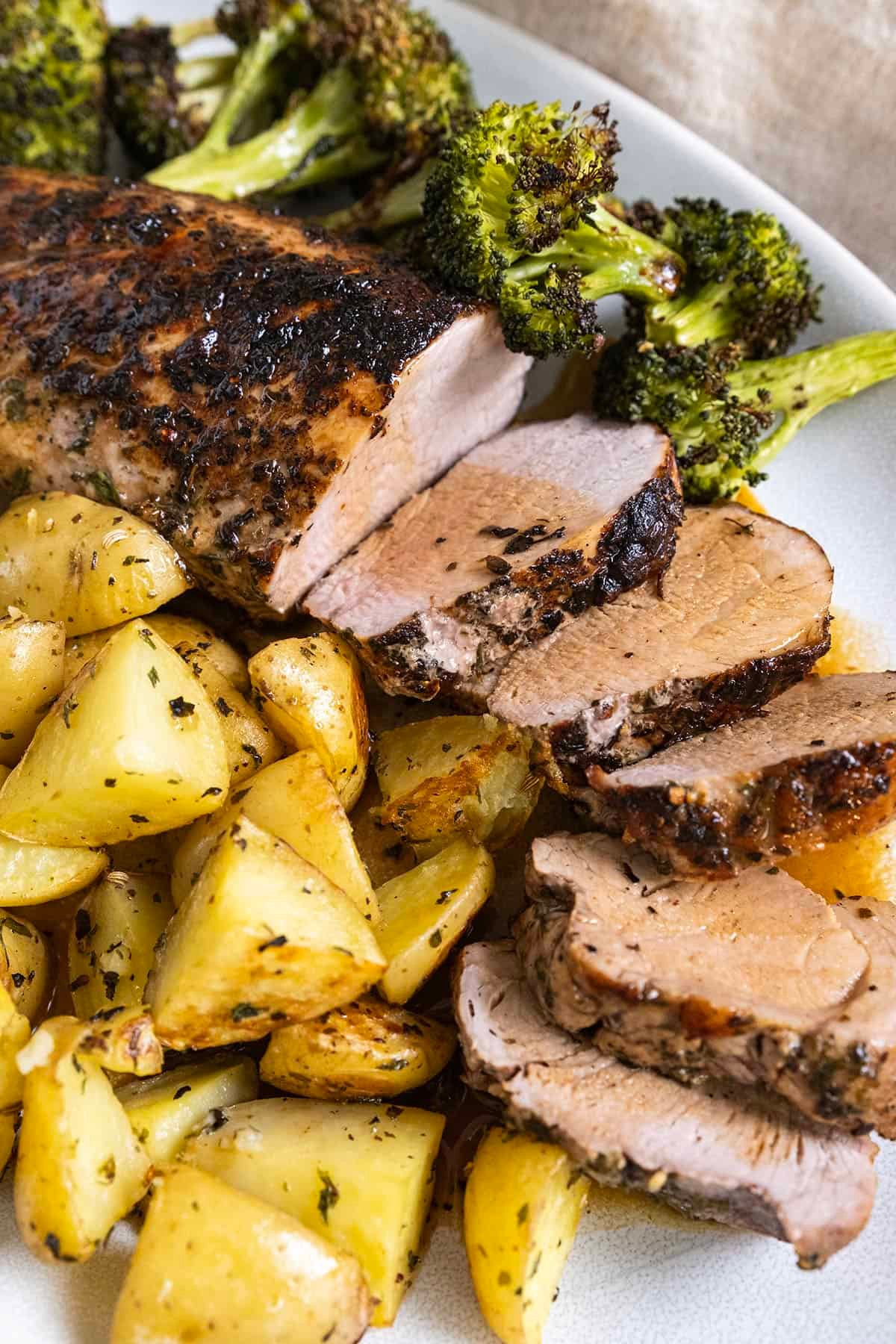 Sliced pork tenderloin served on a plate with roasted potatoes and broccoli.