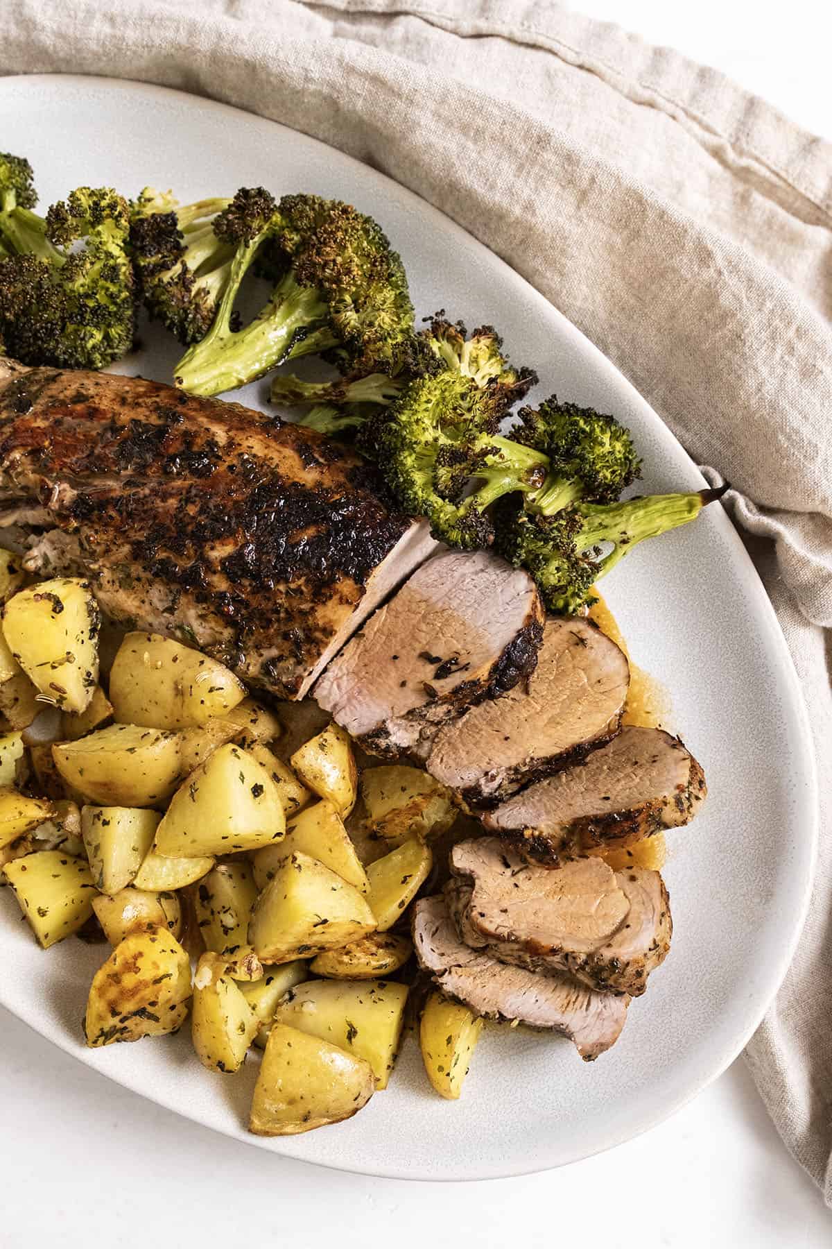 Sliced pork tenderloin served on a plate with roasted potatoes and broccoli.