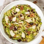 Brussels sprouts salad in a bowl topped with dried cranberries and pecans.