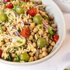 Orzo and garbanzo bean salad with olives, tomatoes, and more in a bowl.