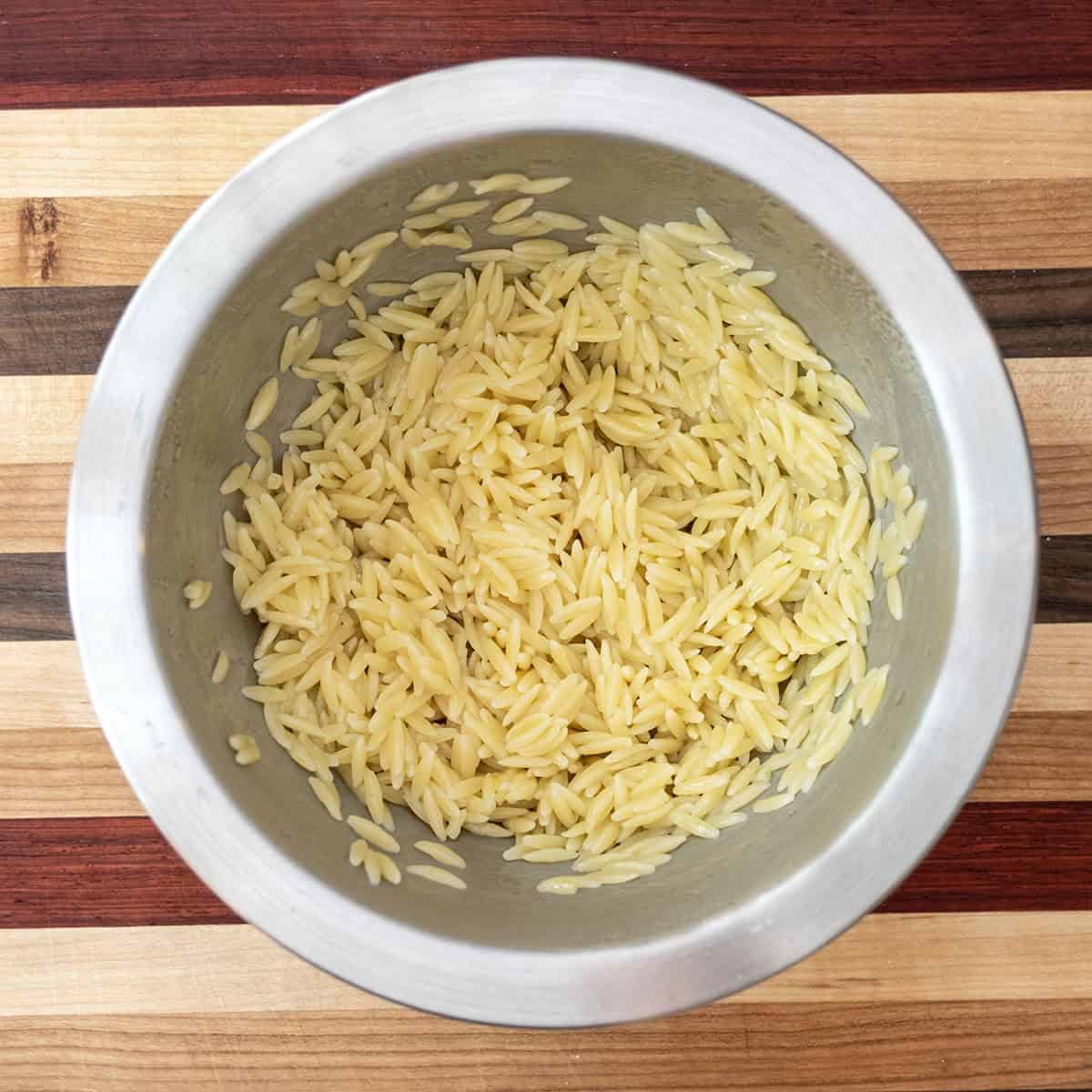 Fresh Orzo Chickpea Salad 5 Cooked orzo pasta being drizzled with olive oil in a small bowl, stirring to prevent sticking as it cools.