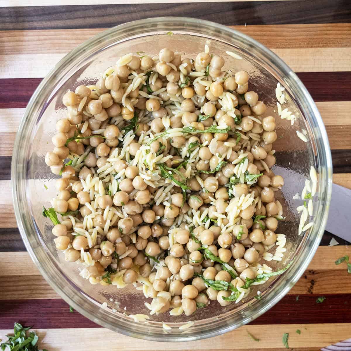 Fresh Orzo Chickpea Salad 7 The dressing being poured over a mixture of orzo, garbanzo beans, and basil in a large bowl, ready to be combined.