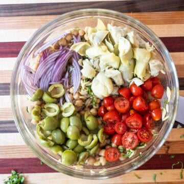 Adding tomatoes, olives, red onion and artichokes into the bowl.