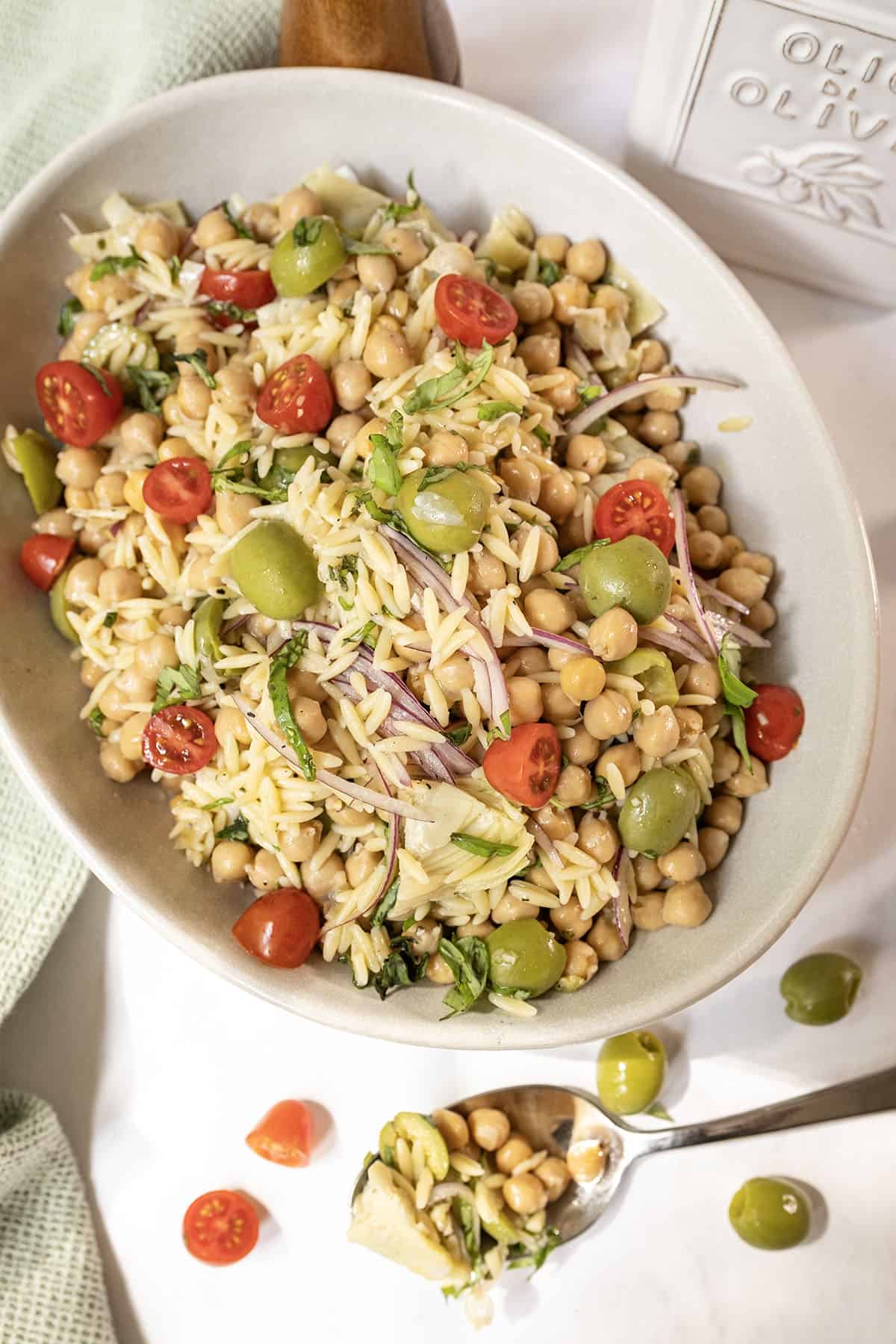 Orzo and garbanzo bean salad with olives, tomatoes, and more in a bowl.