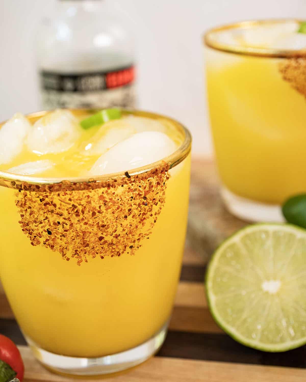 Spicy mango margarita with several jalapenos and limes surrounding it.