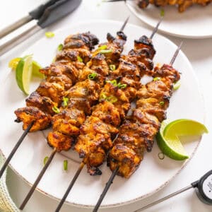 Bang Bang Chicken skewers with limes on the side.