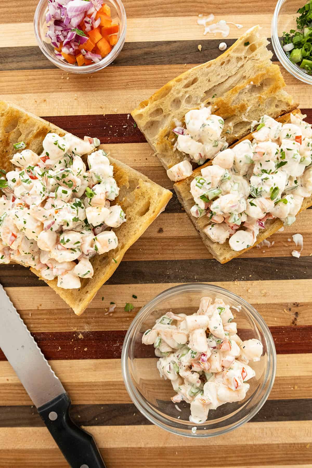 Cold shrimp salad in a bowl with two sandwiches with shrimp salad.