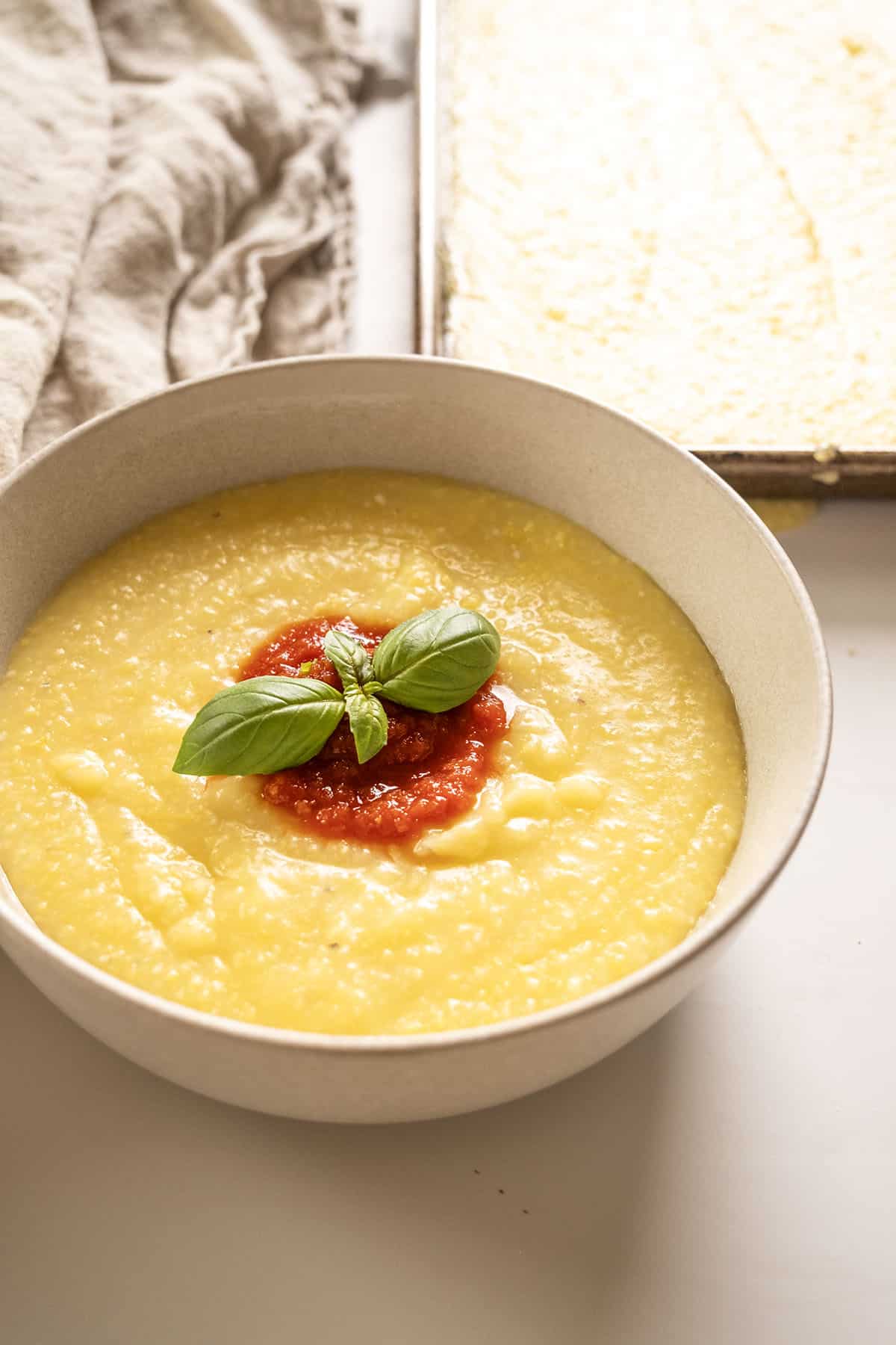 Creamy polenta in a bowl topped with marinara and basil.