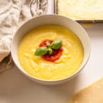 Creamy polenta in a bowl topped with marinara and basil.