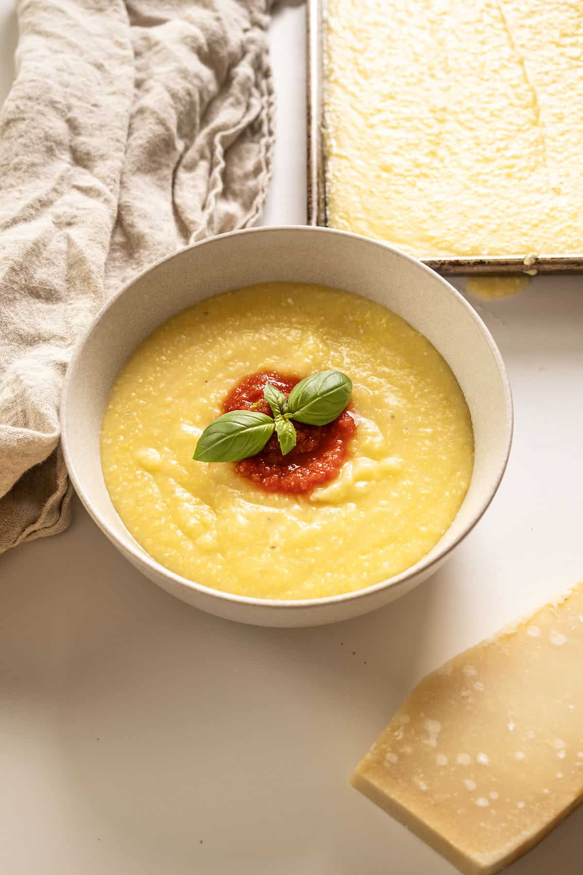 Creamy polenta in a bowl topped with marinara and basil.