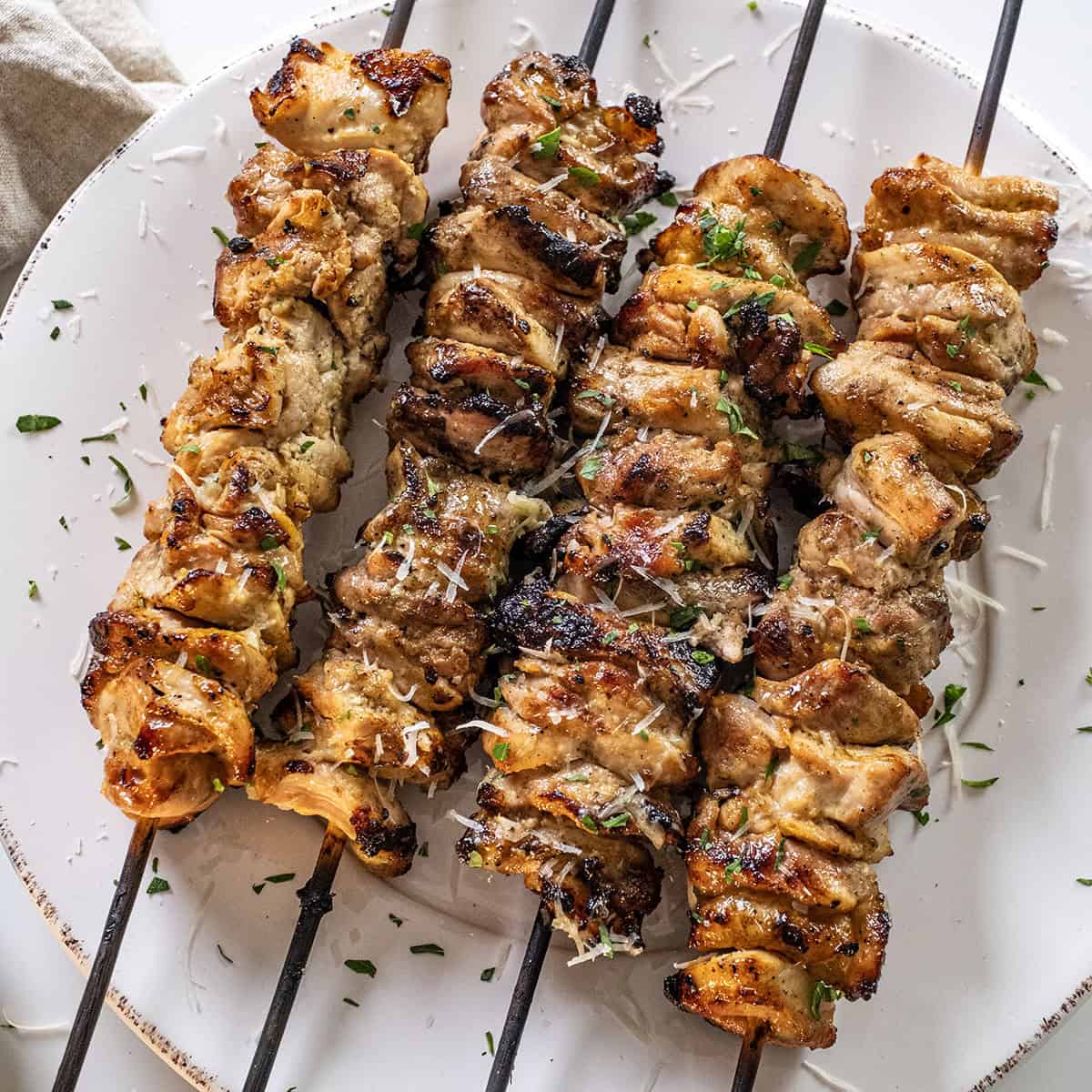 Garlic parm chicken skewers on a plate basted with parm sauce.