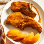 Bourbon peach glazed pork chops on a plate garnished with peaches and extra sauce.
