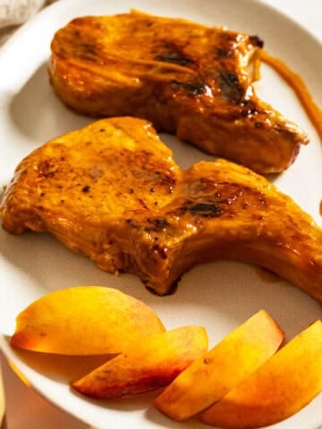 Bourbon peach glazed pork chops on a plate garnished with peaches and extra sauce.
