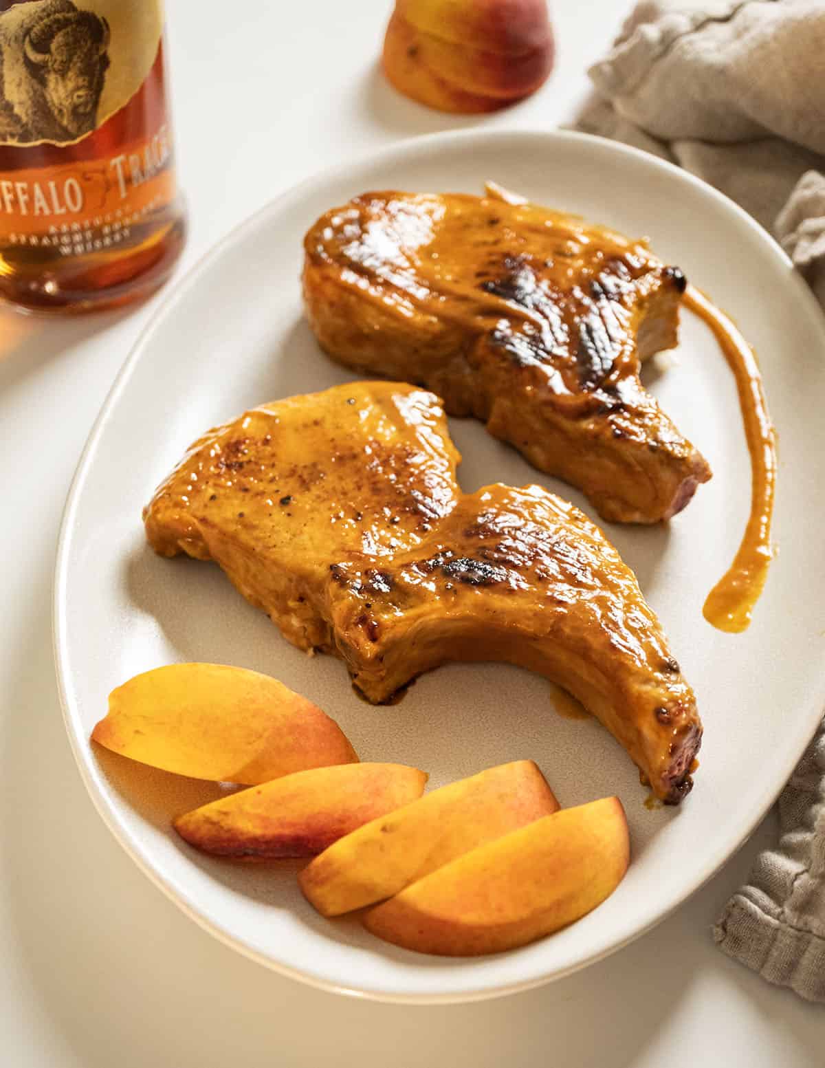 Bourbon peach glazed pork chops on a plate garnished with peaches and extra sauce. 
