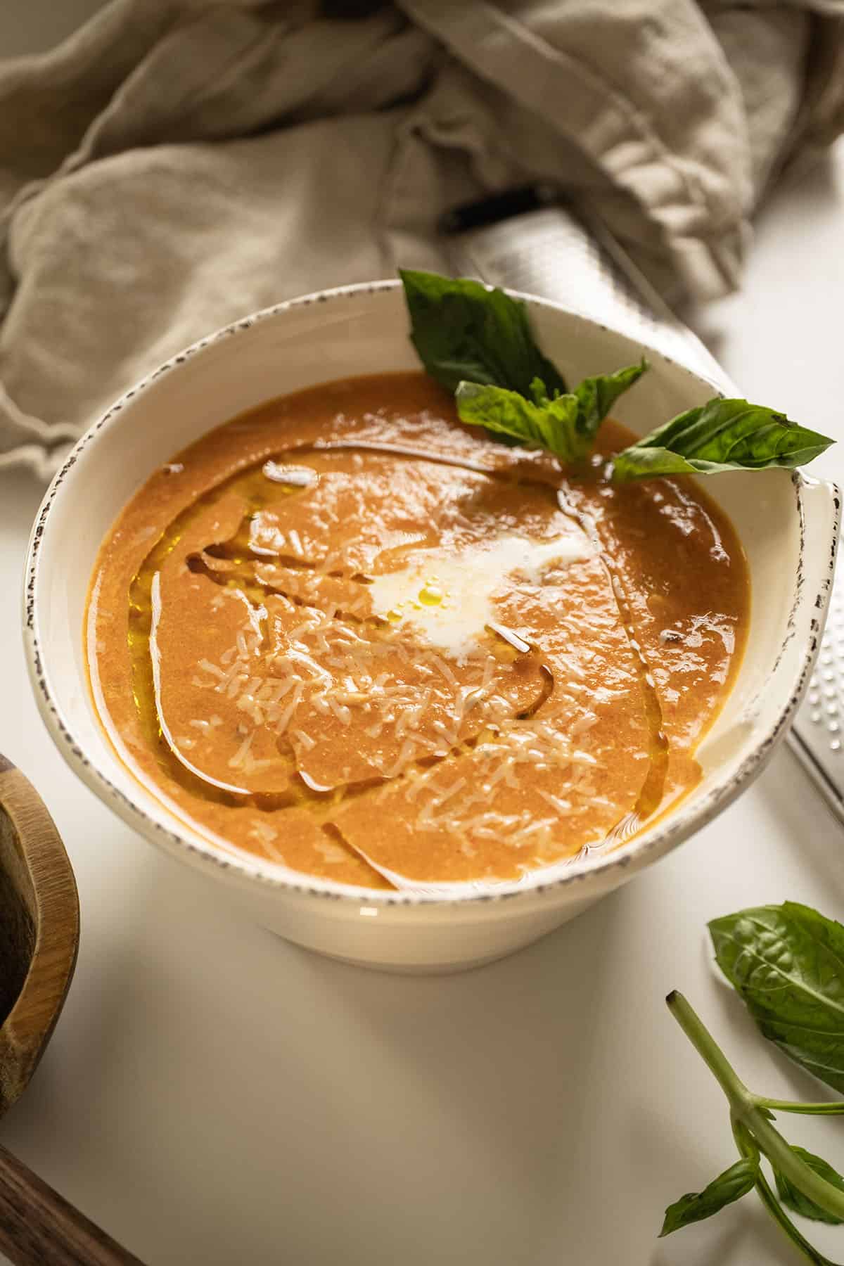 Tomato soup in a bowl topped with cream, olive oil, and basil.