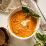 Tomato soup in a bowl topped with cream, olive oil, and basil.