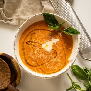 Tomato soup in a bowl topped with cream, olive oil, and basil.