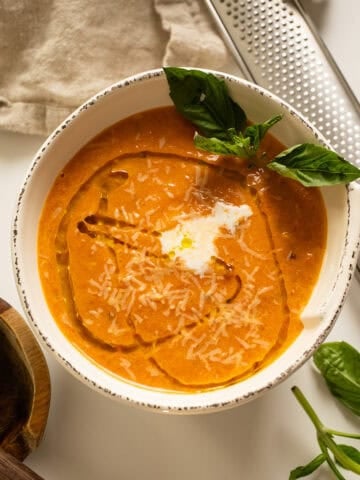 Tomato soup in a bowl topped with cream, olive oil, and basil.