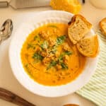 Butternut squash soup with sausage in a bowl and side of crusty Italian bread.