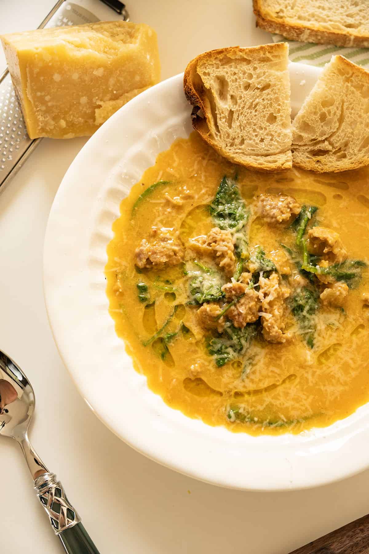 Butternut squash soup with sausage in a bowl and side of crusty Italian bread.