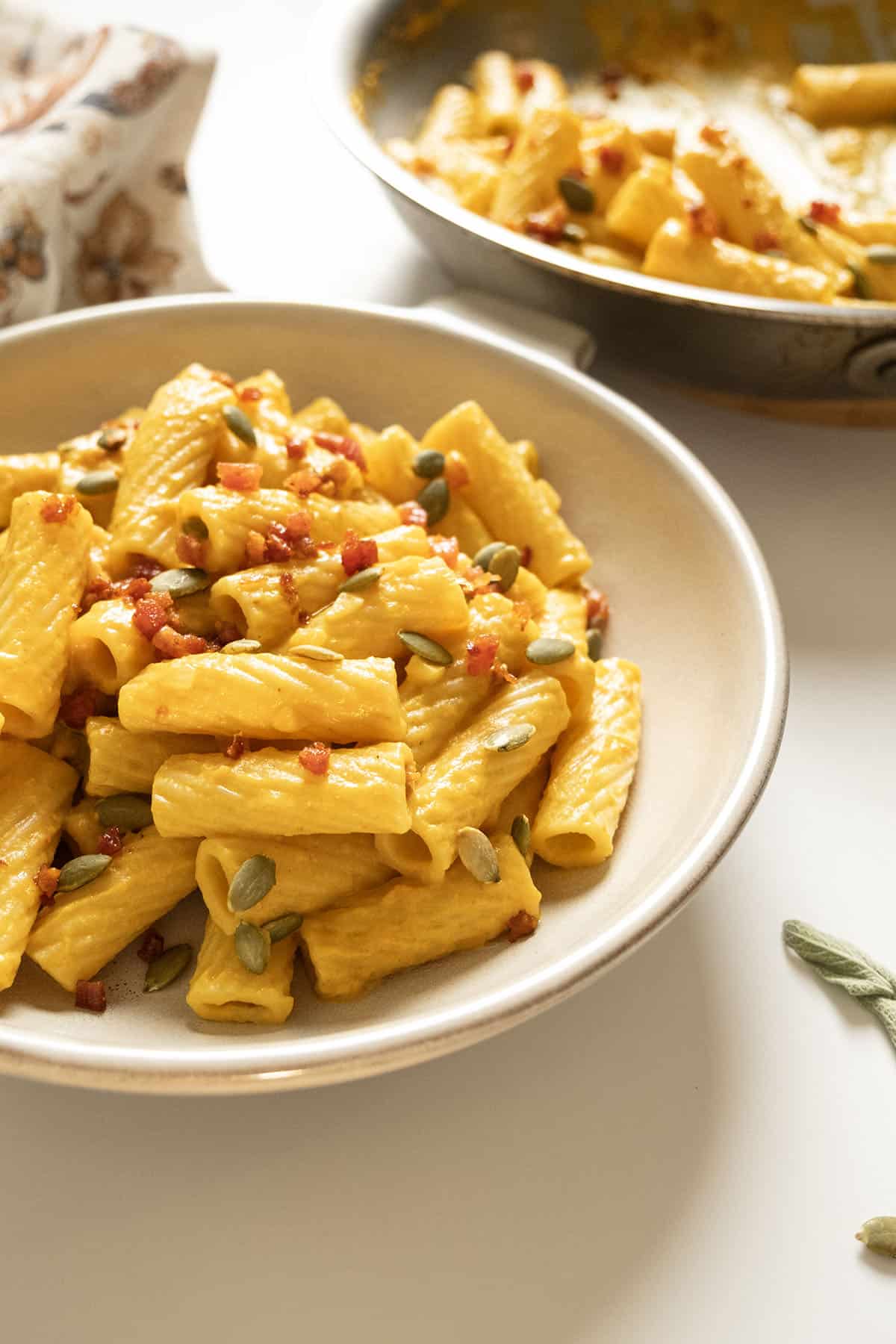 Pumpkin pasta in a bowl topped with pumpkin seeds and pancetta.